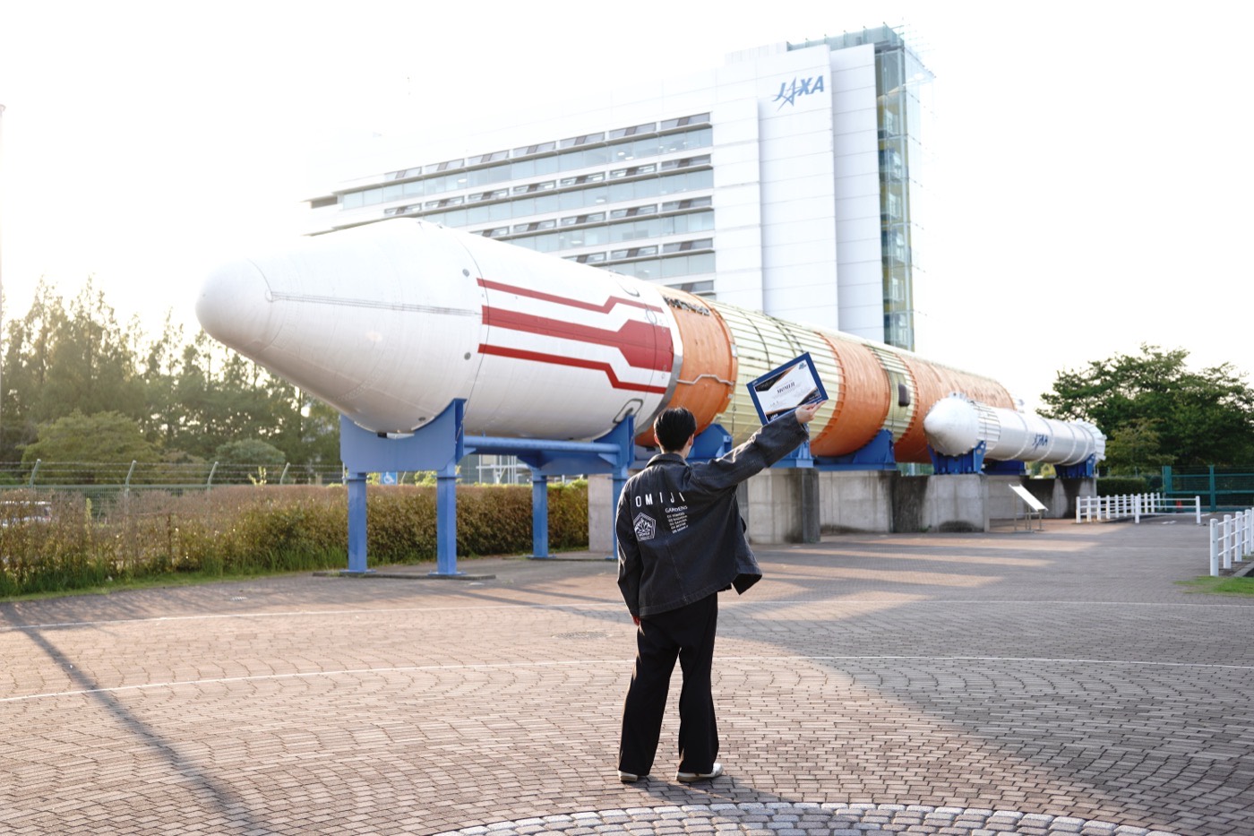 A member of the satellite team holds the MOMIJI certificate of acceptance up toward the rocket displayed at JAXA's Tsukuba Space Center