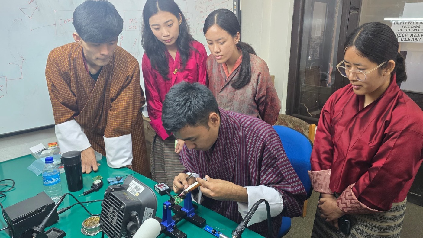 Students at the College of Science and Technology work on the satellite payload, one soldering while others watch